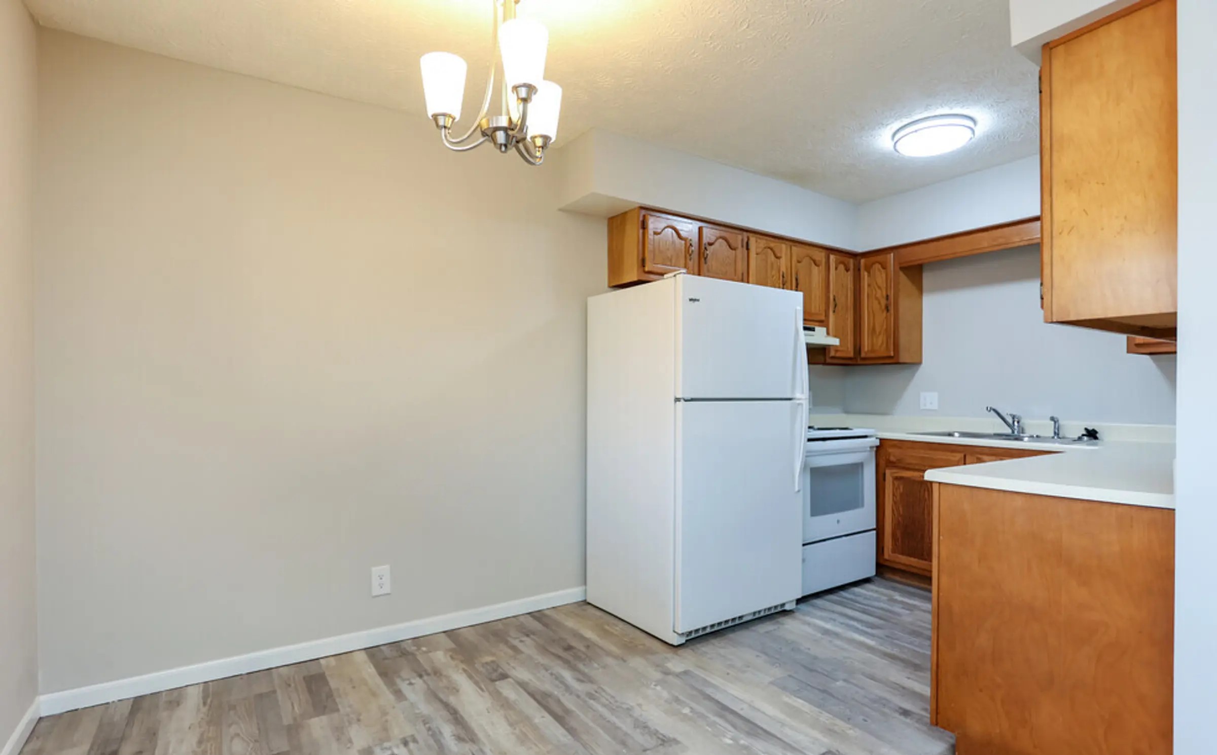 A bright and inviting kitchen and dining area featuring cabinetry, clean countertops, and modern wood-style flooring. The open layout provides a comfortable space for cooking and entertaining, complemented by a cozy dining nook illuminated by a stylish light fixture. Its neutral design makes it easy for you to personalize and create the heart of your new home