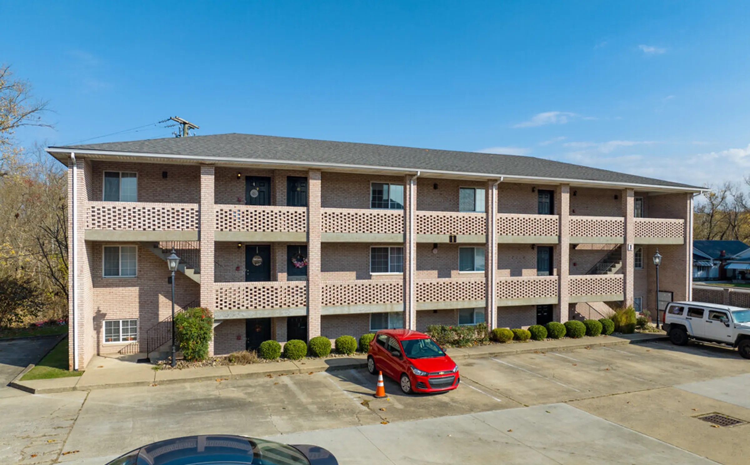 A well-maintained, three-story apartment building featuring attractive brickwork and open, breezy walkways. The façade is complemented by charming lattice-style railings and clean landscaping with manicured shrubs. The convenient on-site parking area provides easy access for residents, making this a practical and inviting place to call home. Its quiet, suburban setting, delivers a sense of comfort and privacy while still being accessible to nearby amenities